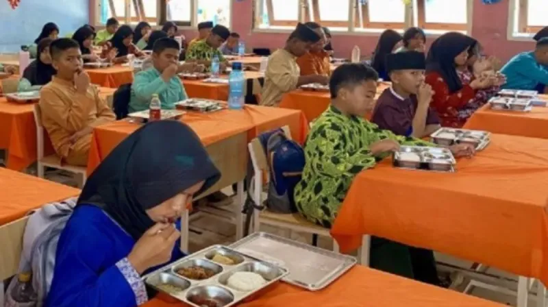 Sejumlah siswa sekolah dasar duduk di dalam kelas sambil menyantap makanan bergizi dalam wadah stainless sebagai bagian dari program Makan Bergizi Gratis.
