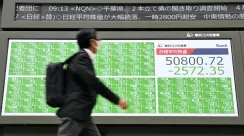 Seorang pria berjalan di depan papan elektronik pergerakan saham di bursa saham Tokyo Jepang.